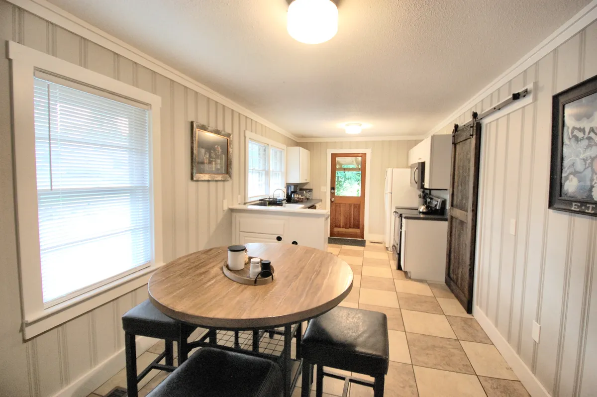A cozy dining area featuring a round wooden table, white cabinetry, a sliding barn door, and framed artwork. The setting feels intimate and is clearly designed for family meals, celebrations, and casual gatherings, as well as everyday activities like morning coffee.