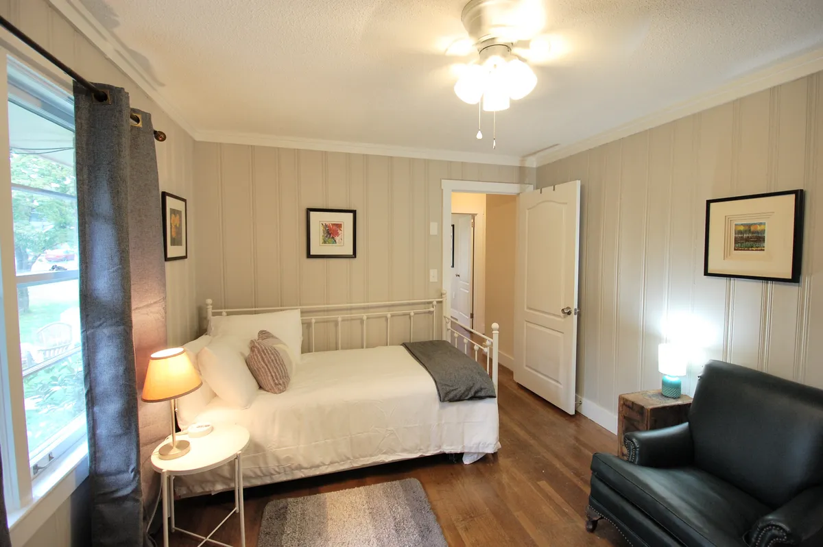 A restful bedroom with a plush bed, an inviting armchair, tasteful artwork, and a soft lamp, all arranged to create a tranquil ambiance. The space feels personal and private, perfect for enjoying peaceful mornings with coffee or unwinding after a day of exploring.
