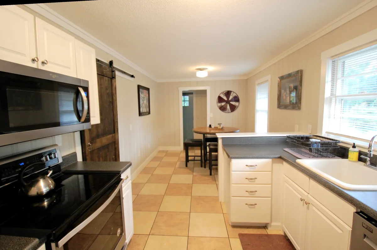 A bright interior scene featuring a kitchen island adjoining a dining table, with windows letting in natural light and a stylish sliding barn door in the background. The setup highlights seamless connectivity between culinary and dining spaces, inviting for meal prep, socializing, and shared experiences.