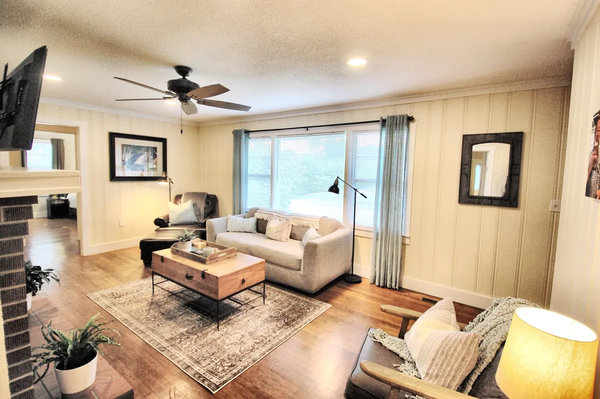 The image showcases a warm, inviting living room where a plush sofa and stylish coffee table are bathed in natural light from a large window. A cozy rug, soft lighting from a nearby floor lamp, and tasteful decor create a perfect space for relaxing, reading, or spending quality time with loved ones.