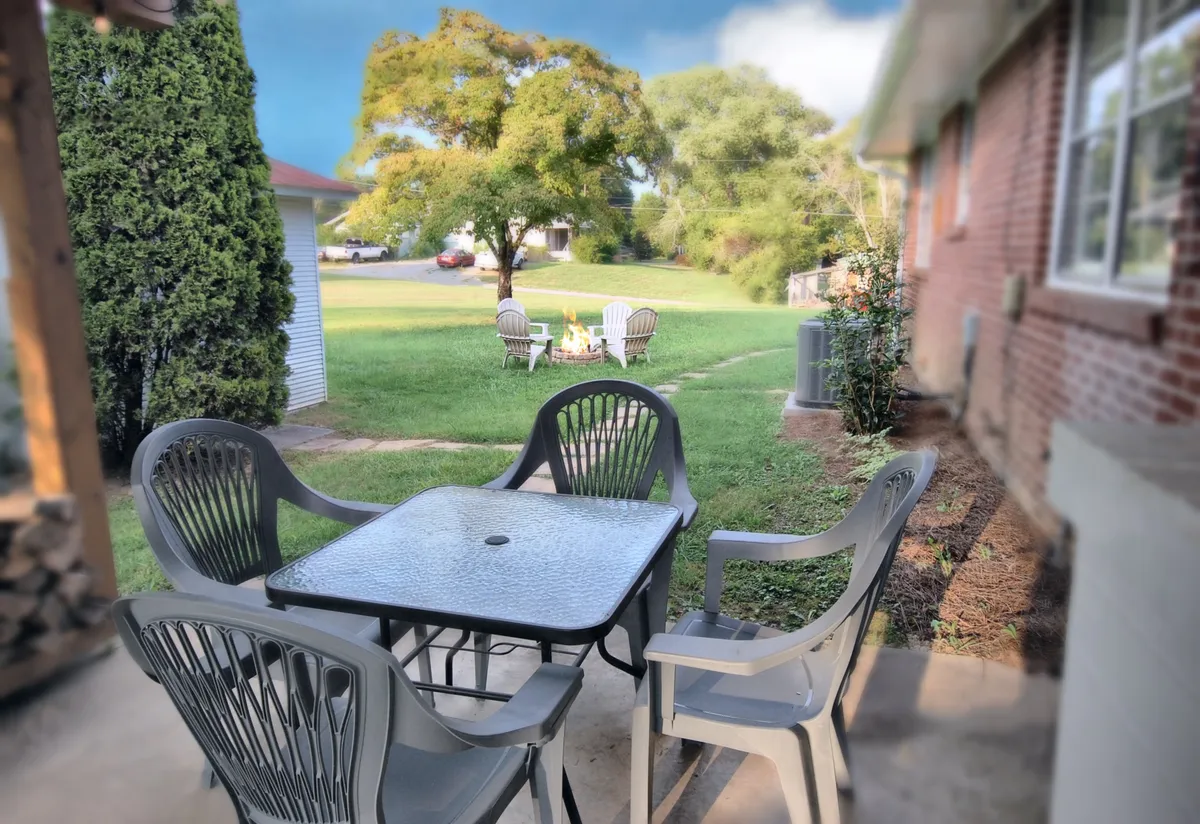 An outdoor dining setup with a table and adirondack chairs arranged on a lush green lawn, adjacent to a fire pit. The area suggests opportunities for al fresco dining, relaxed conversation, and evenings spent outdoors, connecting indoor and outdoor living.
