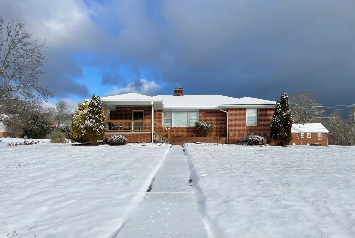 The brick exterior of the house with a snow-dusted front yard, decorative trees, and a clear pathway leading to the door. The porch is visible, hinting at outdoor family gatherings and cozy moments, with an overall ambiance that blends privacy with a sense of community.