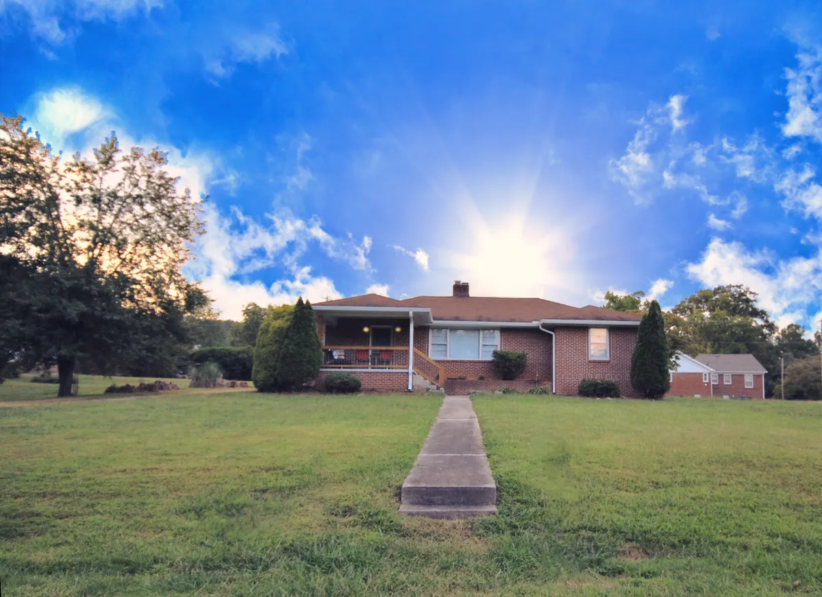 This exterior image showcases the house, its porch, and the pathway leading up, giving a clear view of the approach to the property. The area in front and along the side of the house hints at wide, accessible space suitable for parking vehicles such as motorcycles or boat trailers.