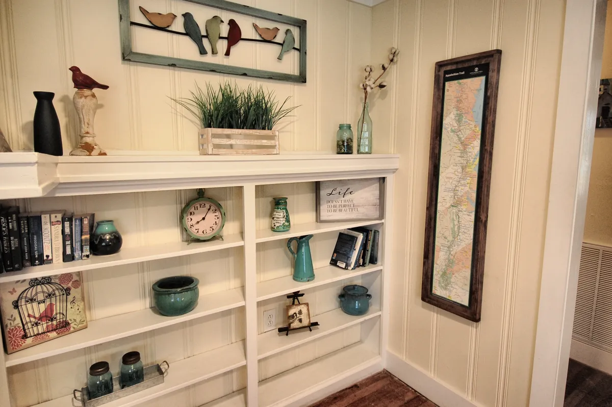 A charming corner with unique bird artwork, shelves filled with books, a vintage-style wall clock, and a decorative map on the wall. The cozy arrangement invites moments of inspiration and contemplation, echoing a creative, folk-inspired atmosphere.