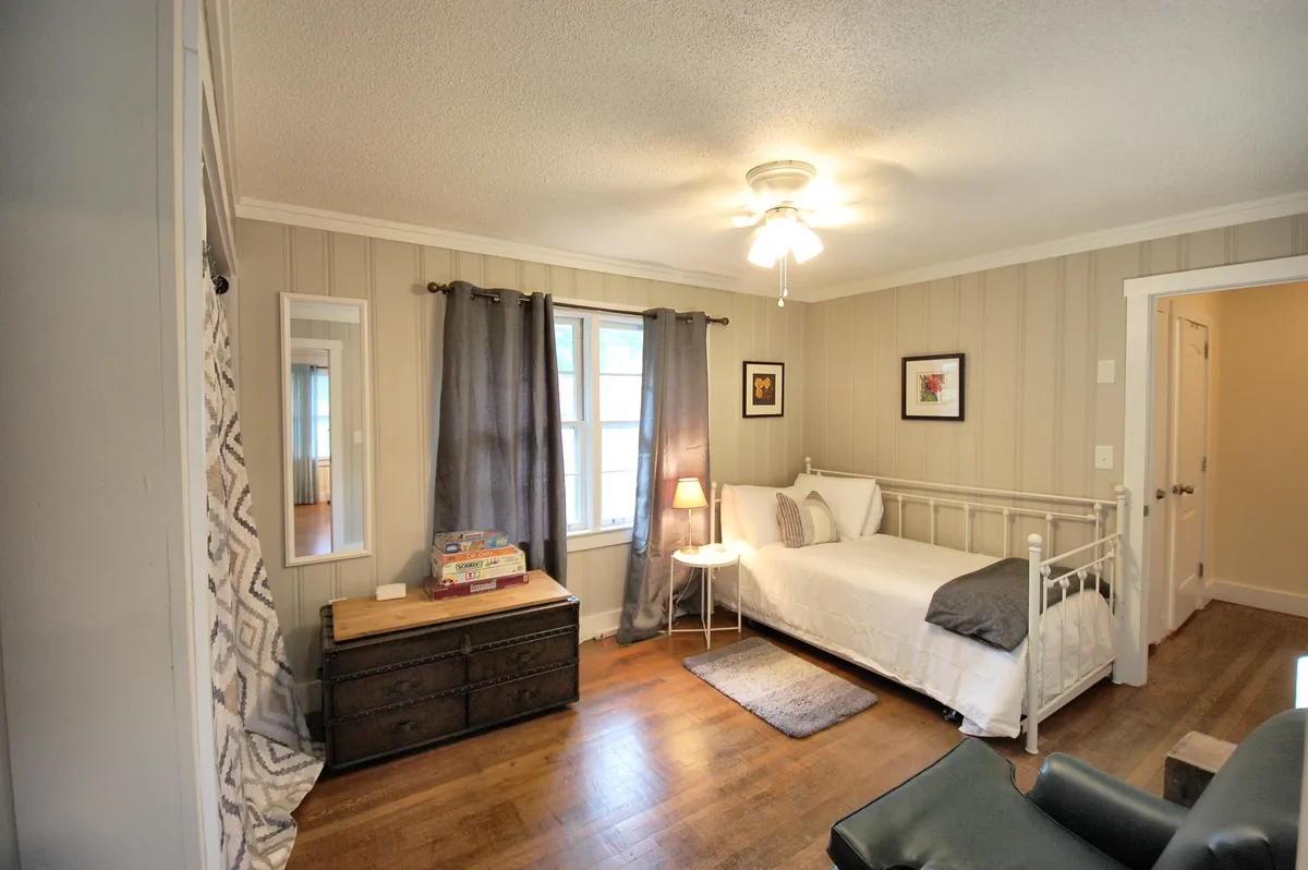 A peaceful bedroom with a large window, soft curtains, and a bed positioned to enjoy the morning light. A chest of drawers and a lamp add a cozy, lived-in feel. The scene emphasizes comfort and a connection to the outdoors, suggesting a refreshing start to dog-friendly explorations.